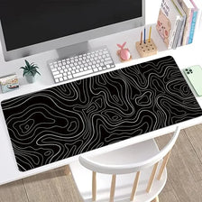 Black topographic map design extended mouse pad with anti-slip base placed on a desk.