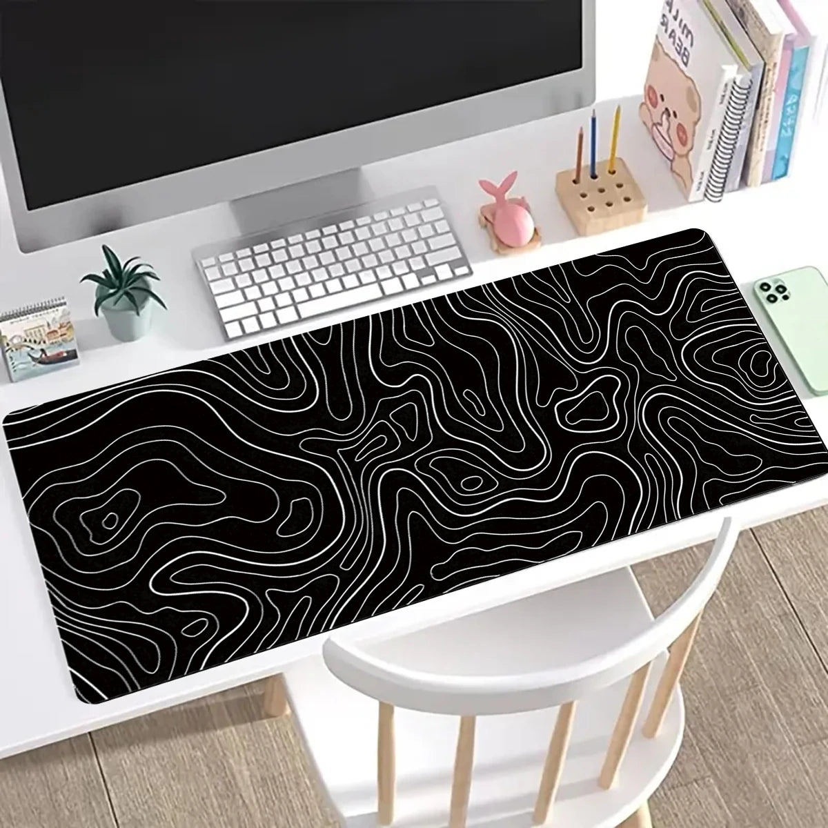Black topographic map design extended mouse pad with anti-slip base placed on a desk.