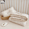 A stack of floral muslin baby blankets and a small white stuffed animal are displayed on a light surface.