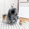 A fluffy gray bunny keychain with a black pom pom tail resting on a black and white grid surface.