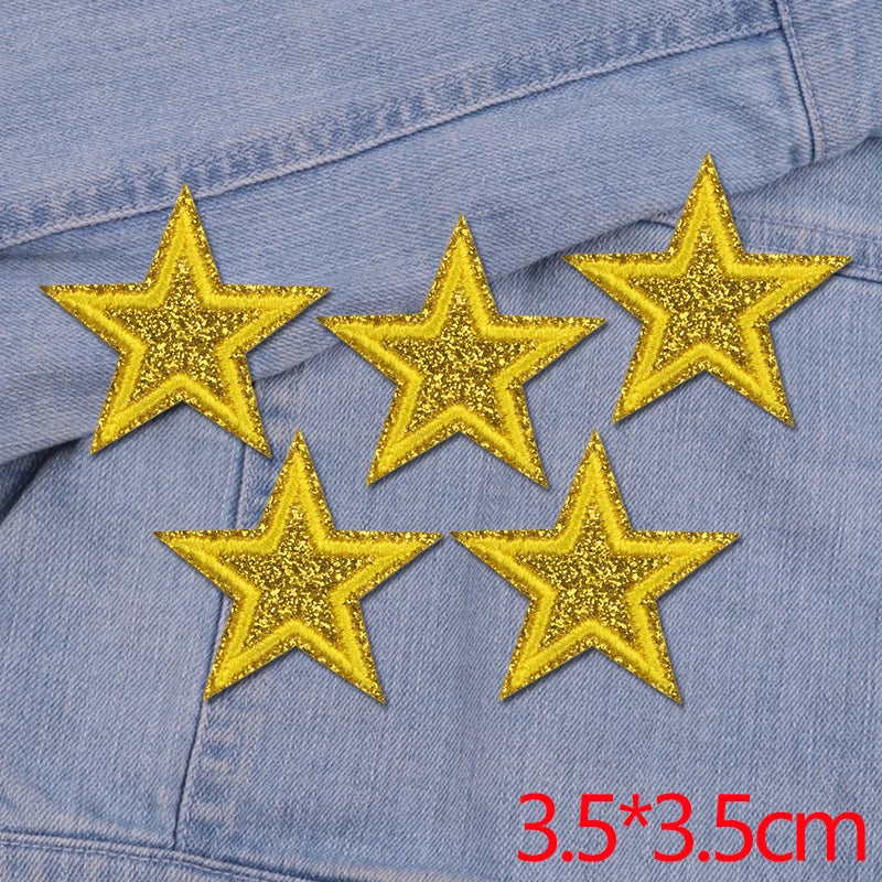 Five gold glitter star iron-on embroidered patches placed on a blue denim fabric.