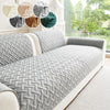 A gray quilted anti-slip sofa cushion displayed on a white sofa with decorative fabric accents.