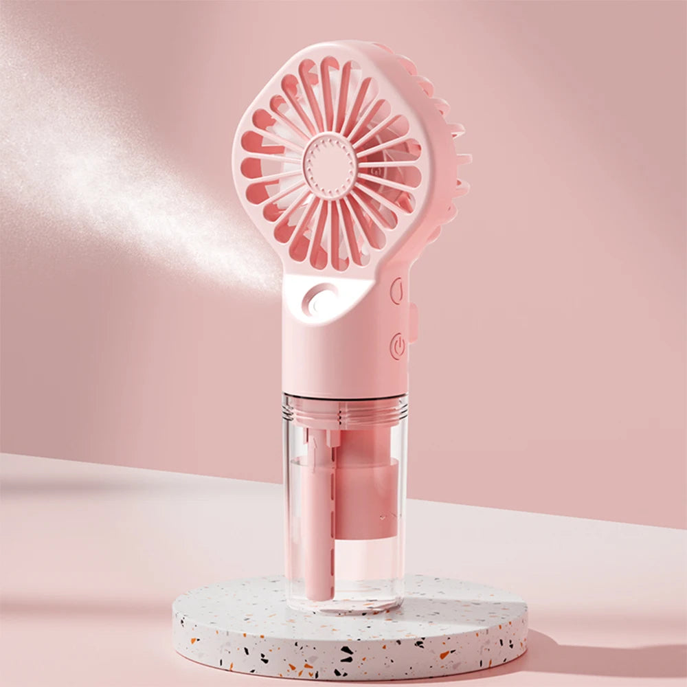 A pink portable USB rechargeable mist fan with a clear container is displayed on a white speckled surface.