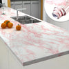 A kitchen countertop with a stainless steel sink and orange fruit, featuring white marble with pink veining.