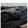A stack of dark gray pure linen bed sheets and pillowcases resting on a wooden box.