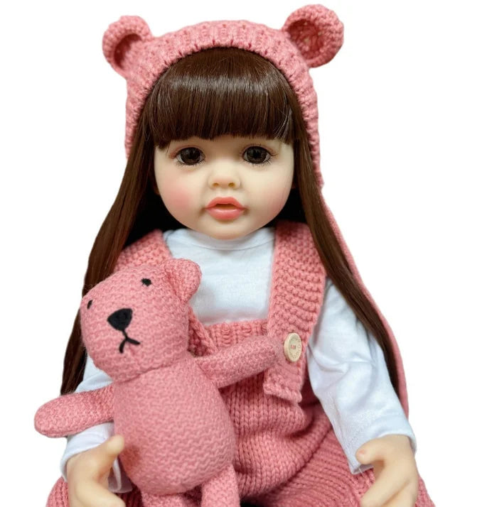 A lifelike silicone baby doll with long dark hair wearing a pink knitted outfit and a matching headband.