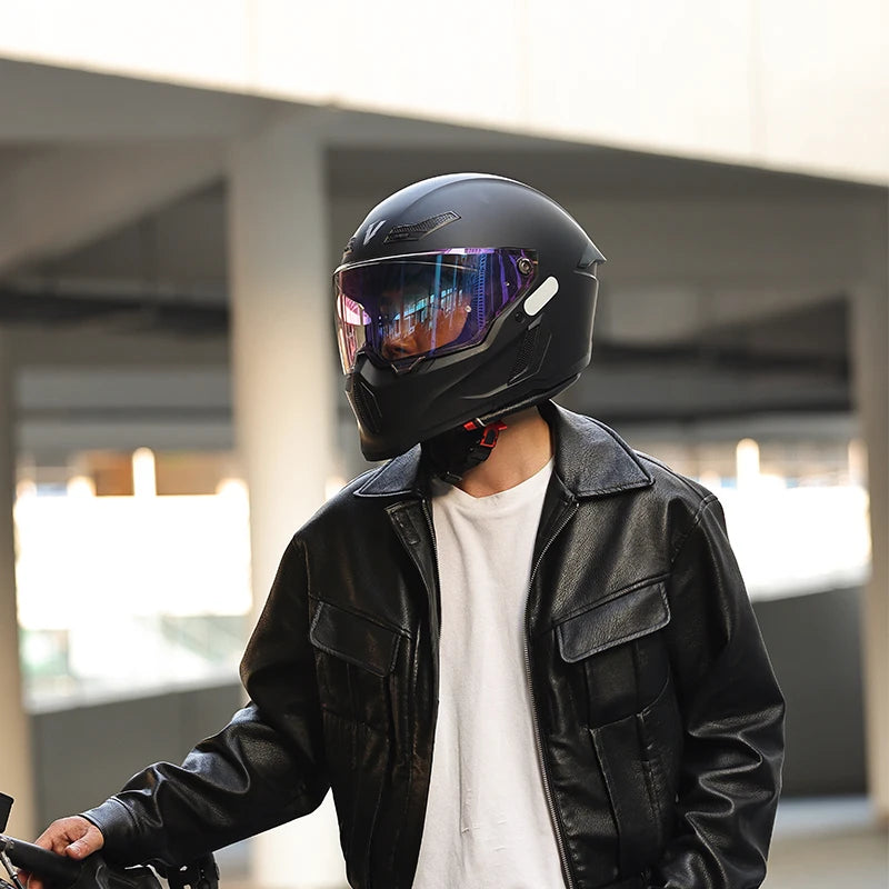 A person wearing a black full-face motorcycle helmet with a tinted visor and a black leather jacket.