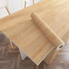 A roll of marble effect self-adhesive PVC film lying on a light wood countertop.