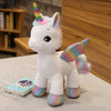 A white unicorn plush toy with a rainbow horn and colorful accents sitting on a table.