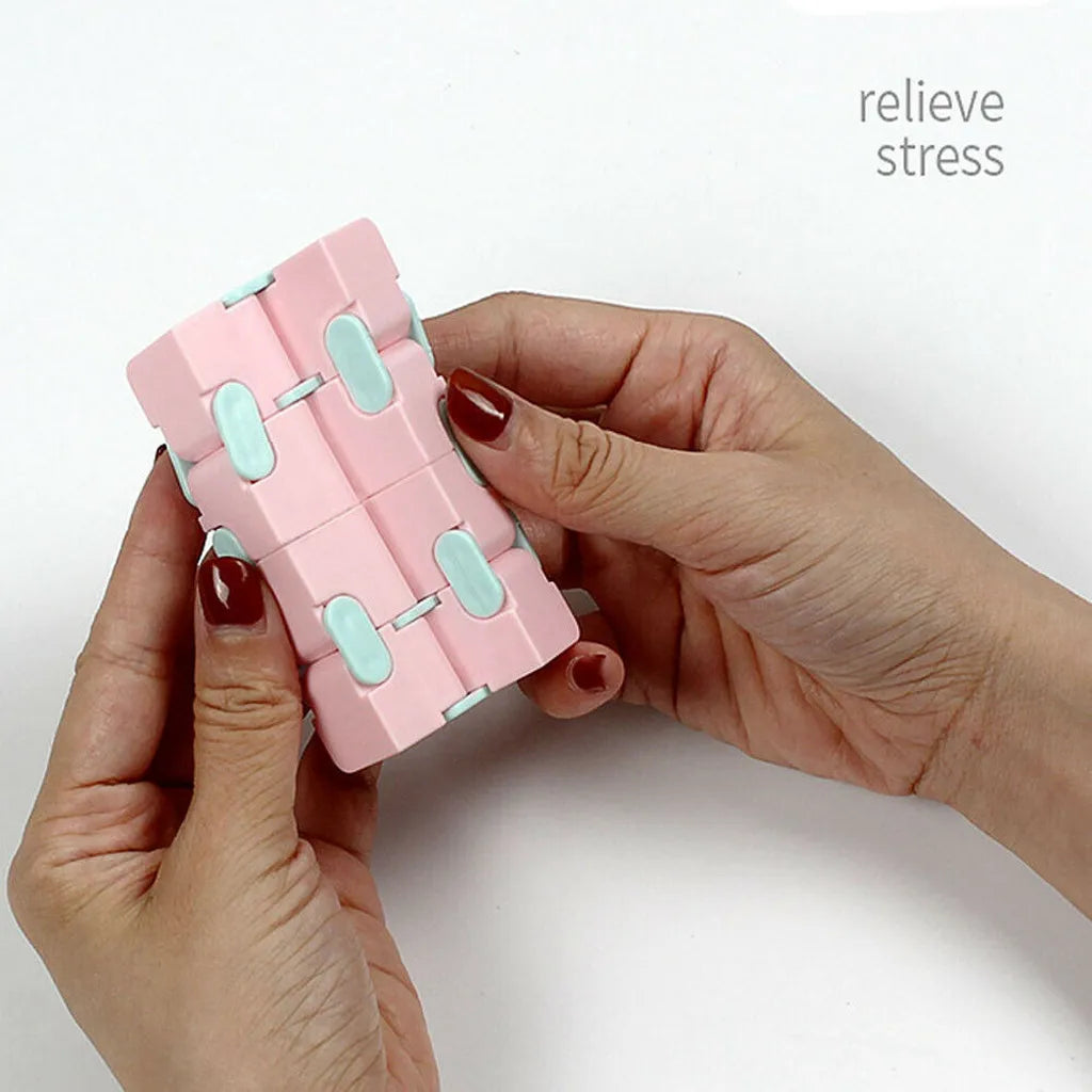 A hand holds a pink infinity magic cube fidget toy with light blue accents for stress relief.