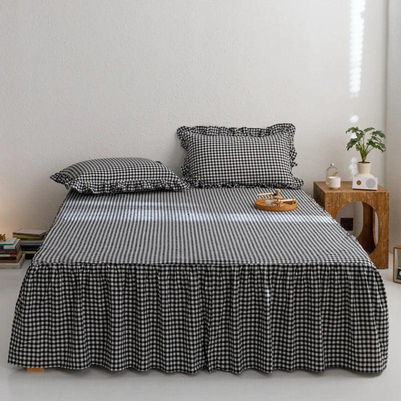 A black and white plaid bed skirt is displayed on a bed, with decorative pillows and a wooden side table in a bright room.