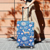 A person is pulling a blue patterned suitcase protector cover on a rolling suitcase outdoors.