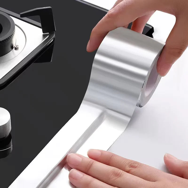 Une main tient un rouleau de ruban de réparation en aluminium argenté à côté d'une cuisinière noire.