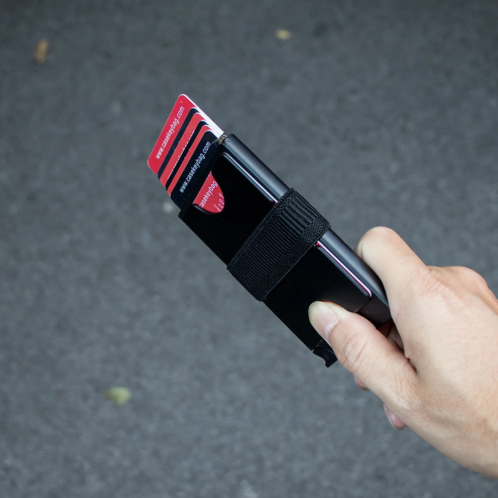 Eine Hand hält einen schwarzen, schlanken RFID-blockierenden Metalldurchschlag-Kartenholder mit einer roten und schwarzen Kar