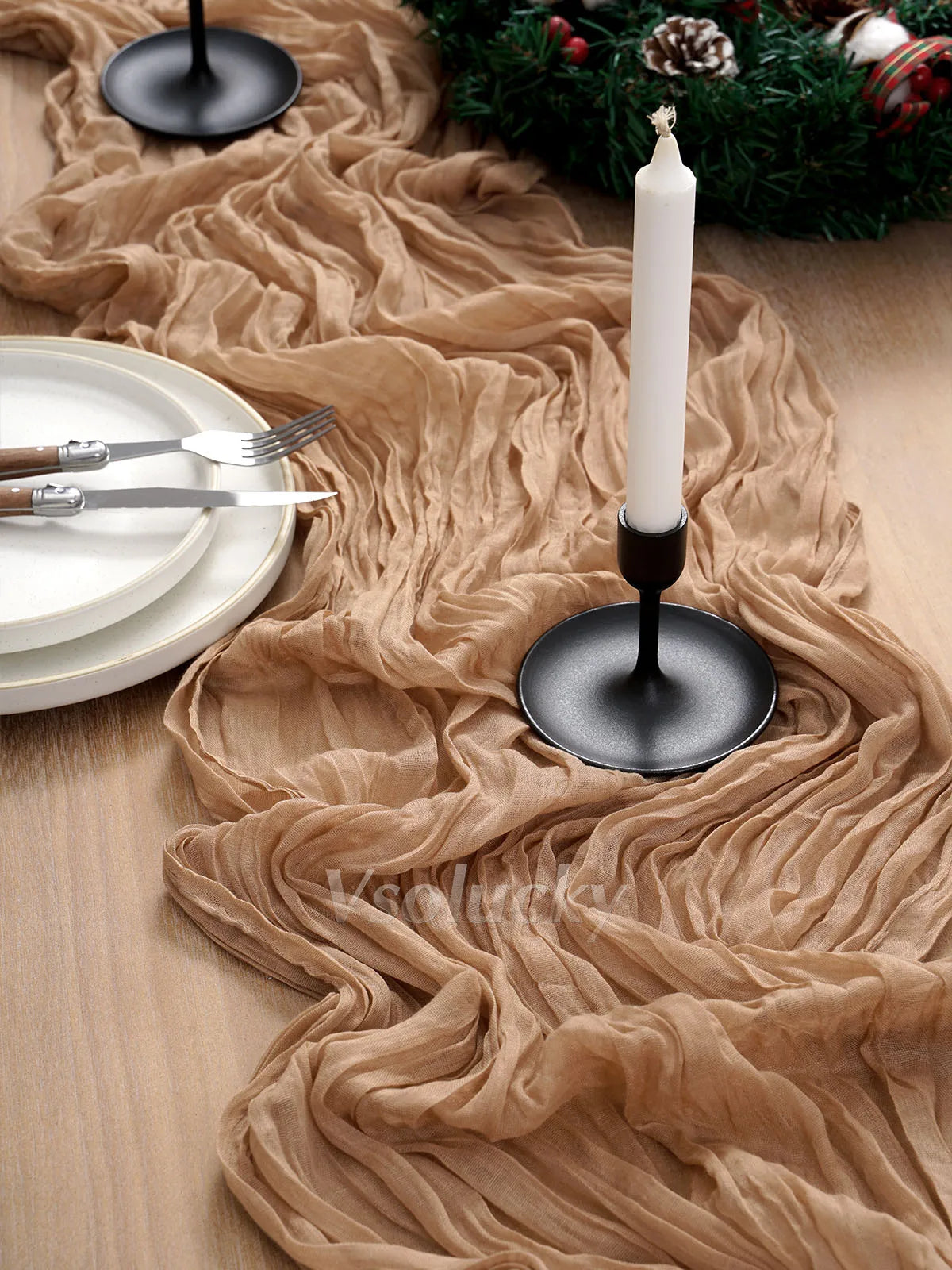 A beige crinkle gauze table runner draped across a wooden surface with a white candle in a black holder.
