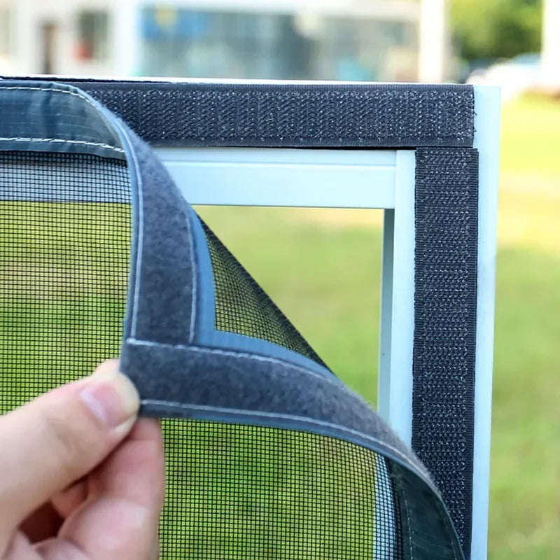 A hand is adjusting a black and gray reusable self-adhesive mosquito window screen frame.