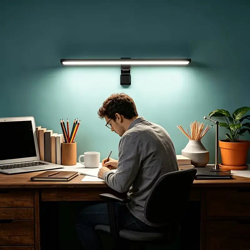A man works at a desk illuminated by an overhead USB powered anti-glare monitor light bar.