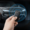 A hand holds a carbon fiber car key cover near the headlight of a dark car, with a blue circular graphic overlay.