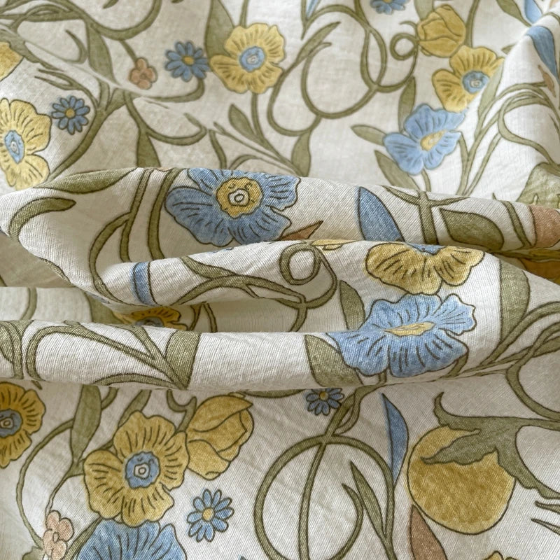 A close-up of a cream fabric featuring a botanical pattern of yellow and blue flowers on a light background.