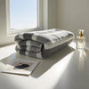 A stack of gray and white striped quick-dry bath towels next to a glass perfume bottle on a white windowsill.