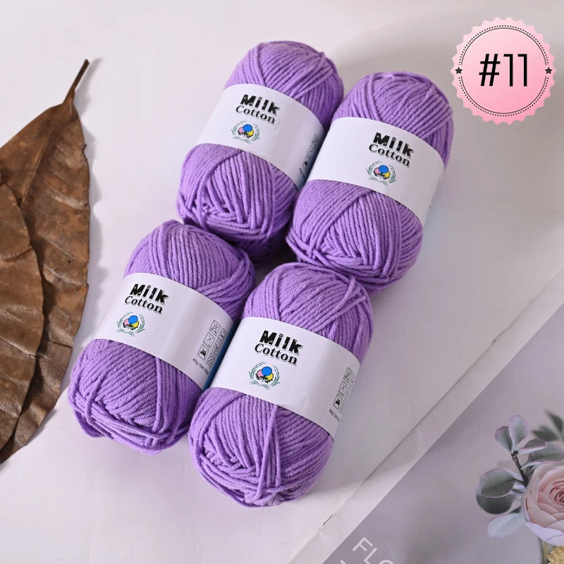 Purple Milk Cotton yarn skeins displayed on a white surface next to a dried leaf.