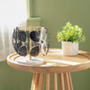 A gold-toned sunglasses organizer stand with multiple slots rests on a light wooden table.