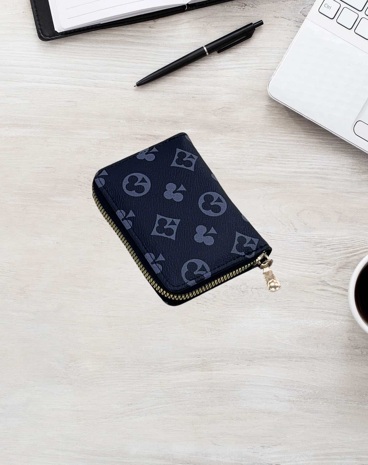 A dark blue compact zippered card holder wallet resting on a light wooden surface next to a pen and a laptop.