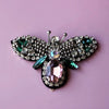 A handcrafted rhinestone bee sew-on patch featuring iridescent green and silver stones on a dark background.