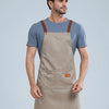 A man wearing a beige waterproof kitchen apron with brown straps and a gray t-shirt.