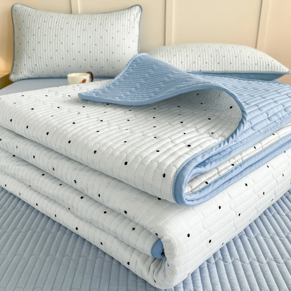 A stack of light blue and white quilted bedspreads and pillows on a bed.
