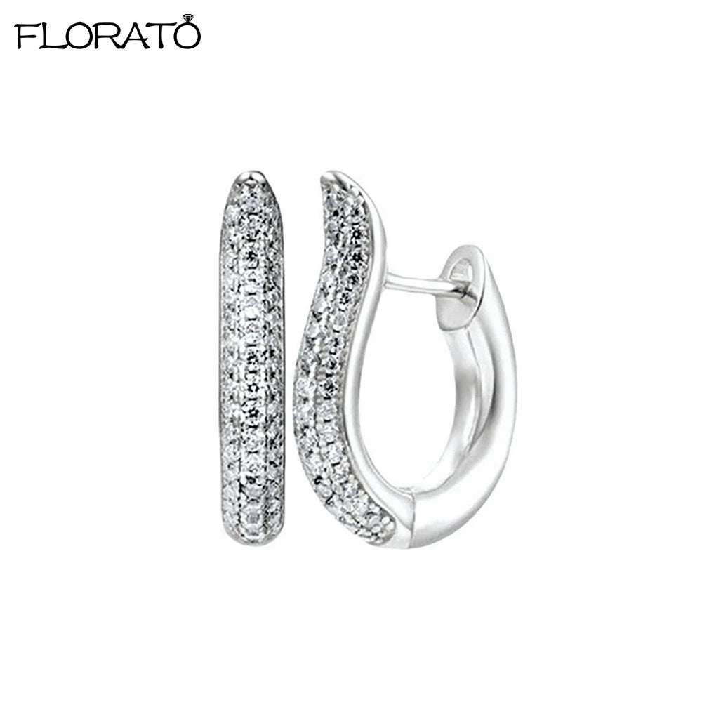 A pair of minimalist cubic zirconia huggie hoop earrings shown against a white background.