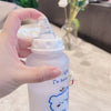 A hand holds a white water bottle with a blue bear design and a clear silicone lid.