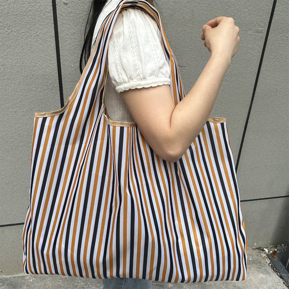 A person holds a striped tote bag with vertical black, white, and brown stripes against a gray background.