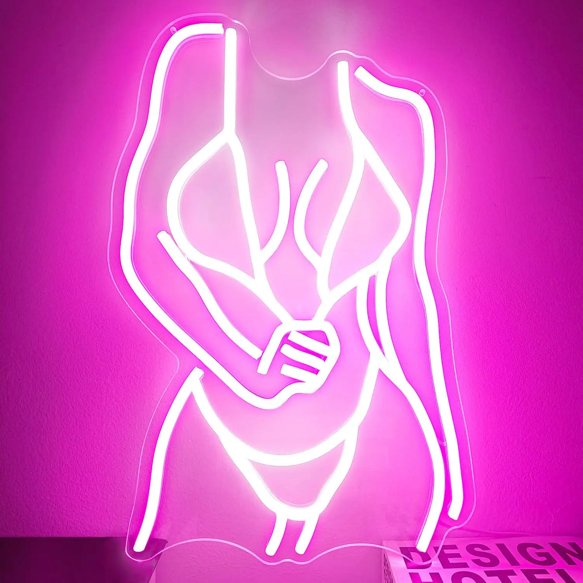 A glowing pink neon silhouette of a female torso and arms on a wall.