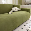 A lime green stretch jacquard sofa cover with a white knitted pillow and black accents in a bright room.