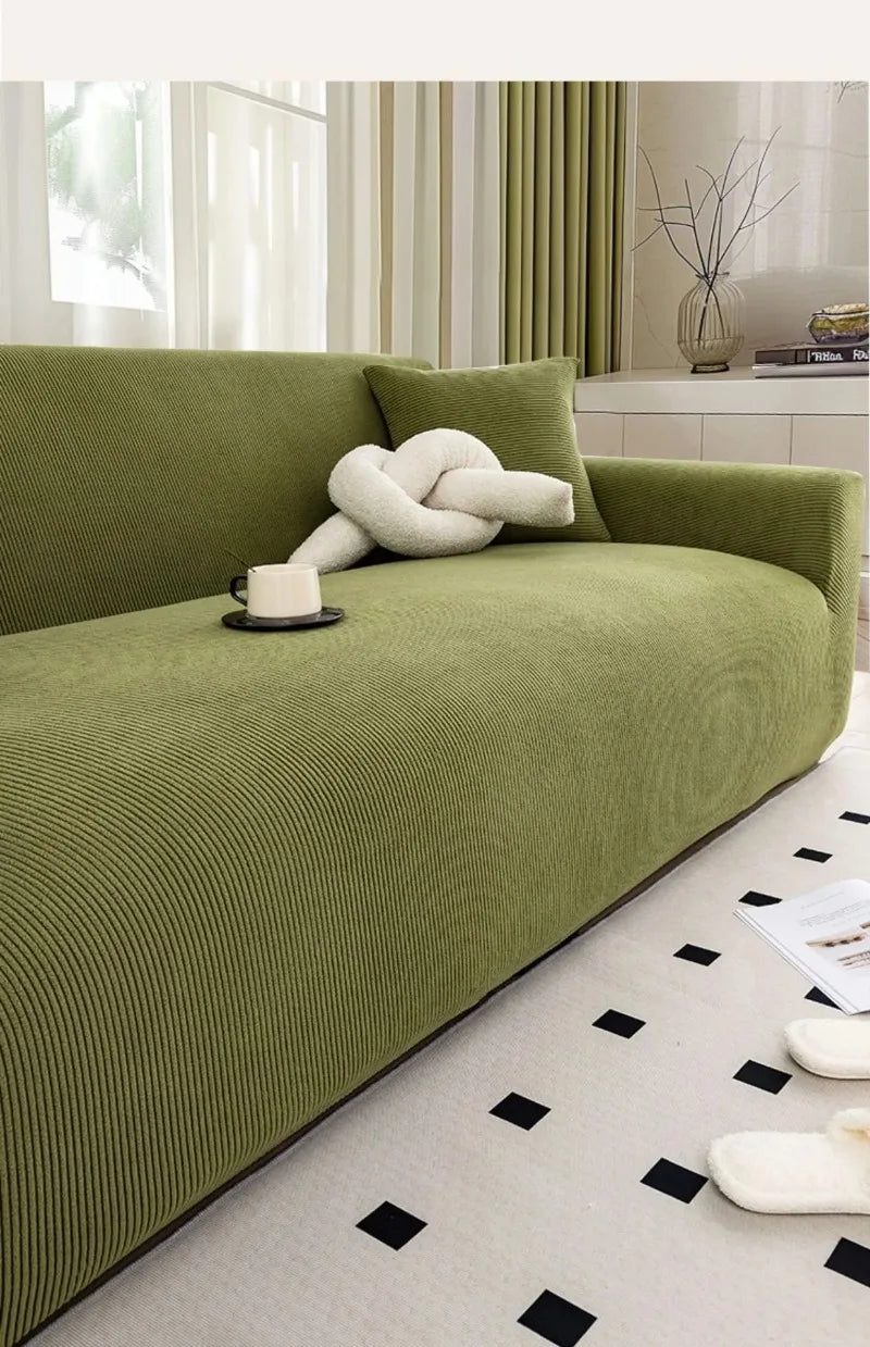 A lime green stretch jacquard sofa cover with a white knitted pillow and black accents in a bright room.