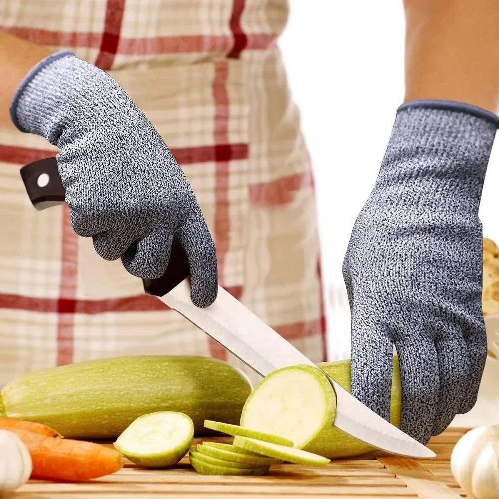 A hand wearing blue cut-resistant work gloves is slicing fresh vegetables like cucumbers and carrots on a wooden board.