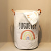 A white fabric storage basket with a rainbow print and leather handles.