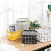 A collection of gray, black, and white woven storage baskets on a wooden table next to a potted plant.