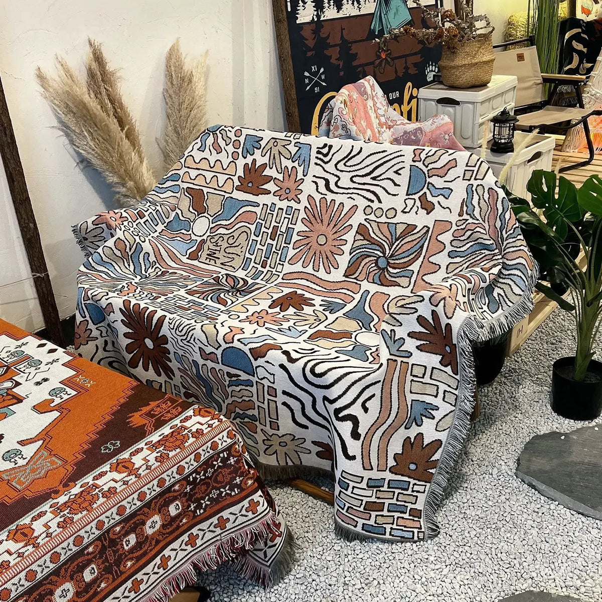 A patterned bohemian jacquard woven throw blanket draped on a sofa next to other textiles.