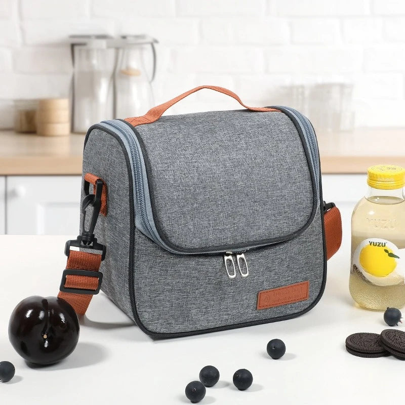 A gray insulated lunch bag with an orange strap is shown on a white surface.