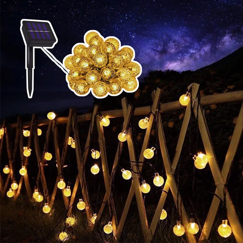 Solar-powered crystal globe string lights illuminating a wooden fence and landscape at night.