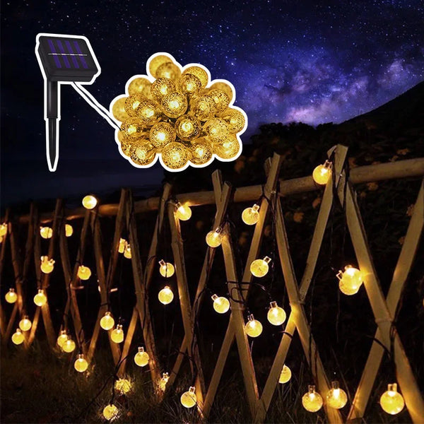 Solar-powered crystal globe string lights illuminating a wooden fence and landscape at night.