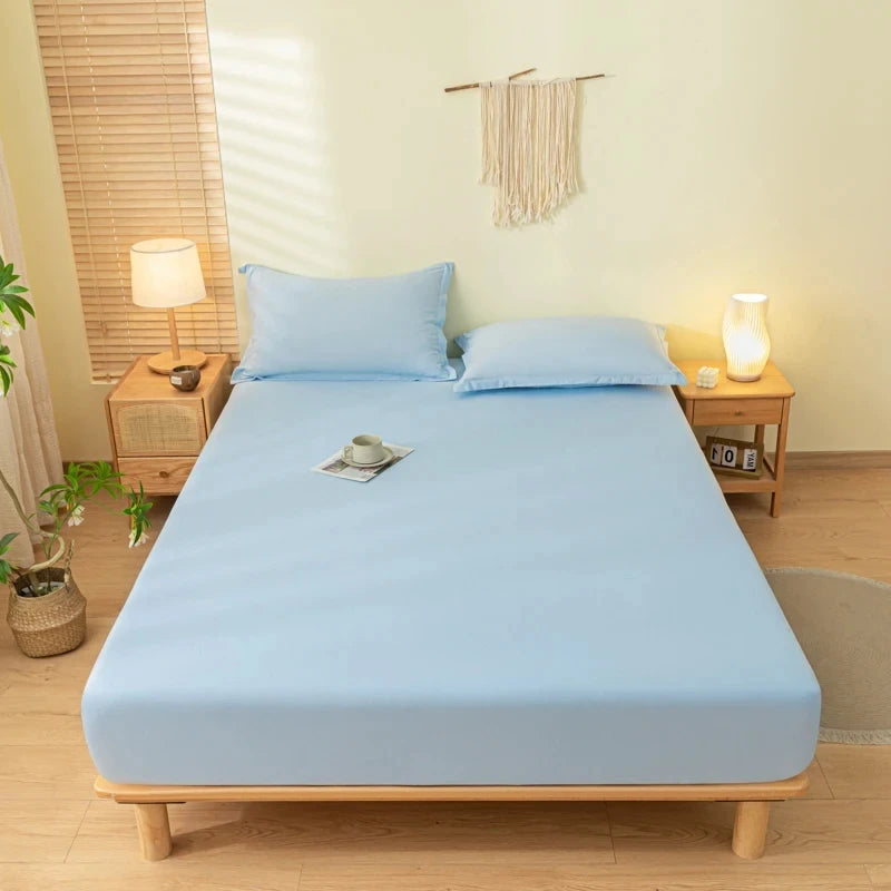 A light blue fitted bed sheet set with pillowcases is laid out on a wooden bed frame in a bright bedroom.