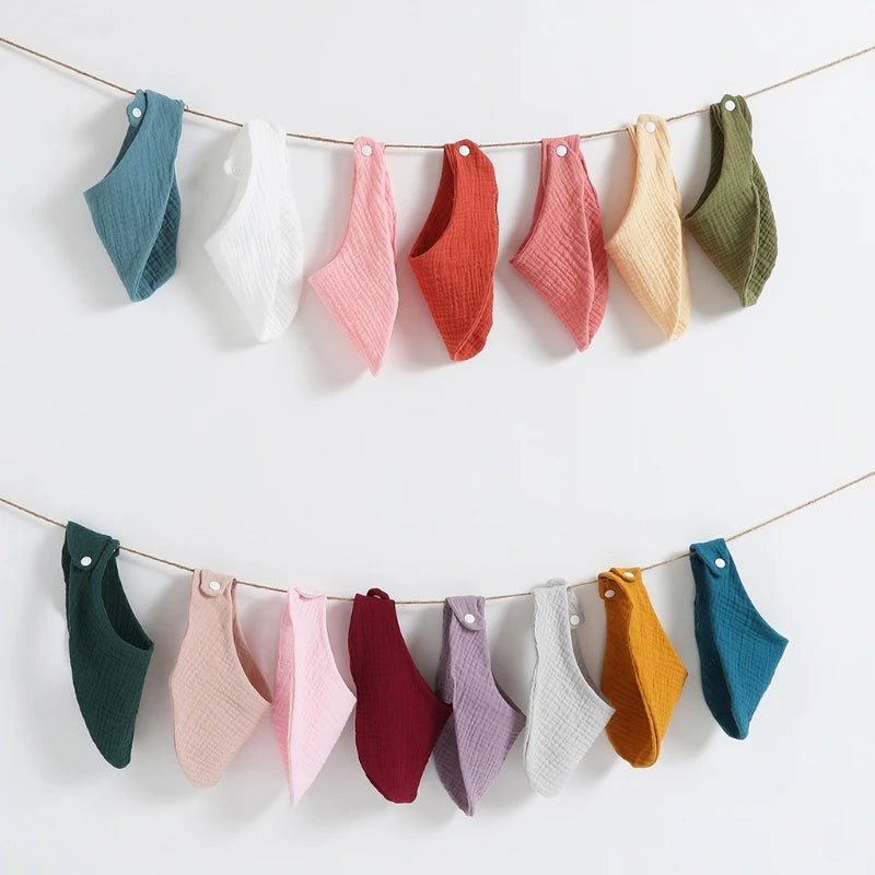 A collection of colorful organic cotton muslin baby bibs hanging on a line.