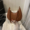 A brown textured crossbody bag with a gold chain strap is displayed against a white shirt.
