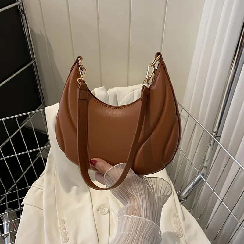 A brown textured crossbody bag with a gold chain strap is displayed against a white shirt.