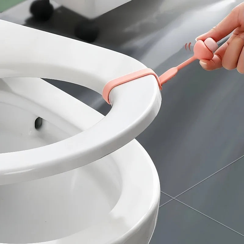 A hand is using a silicone toilet seat lifter with a pull ring to lift the seat on a white toilet.