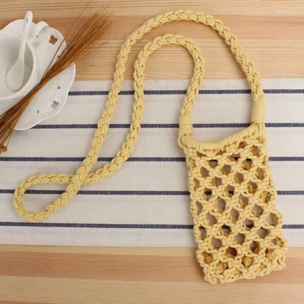 A light yellow crochet crossbody phone bag with a braided strap is displayed on a striped cloth.