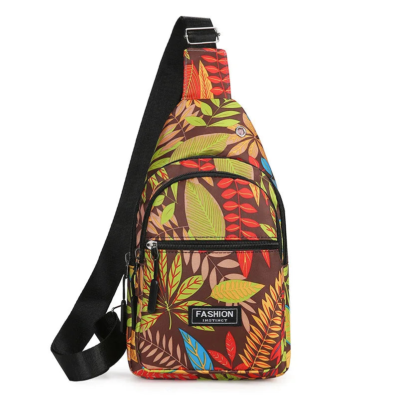 A brown and green leaf print sling crossbody bag with black strap and multiple zippered pockets.